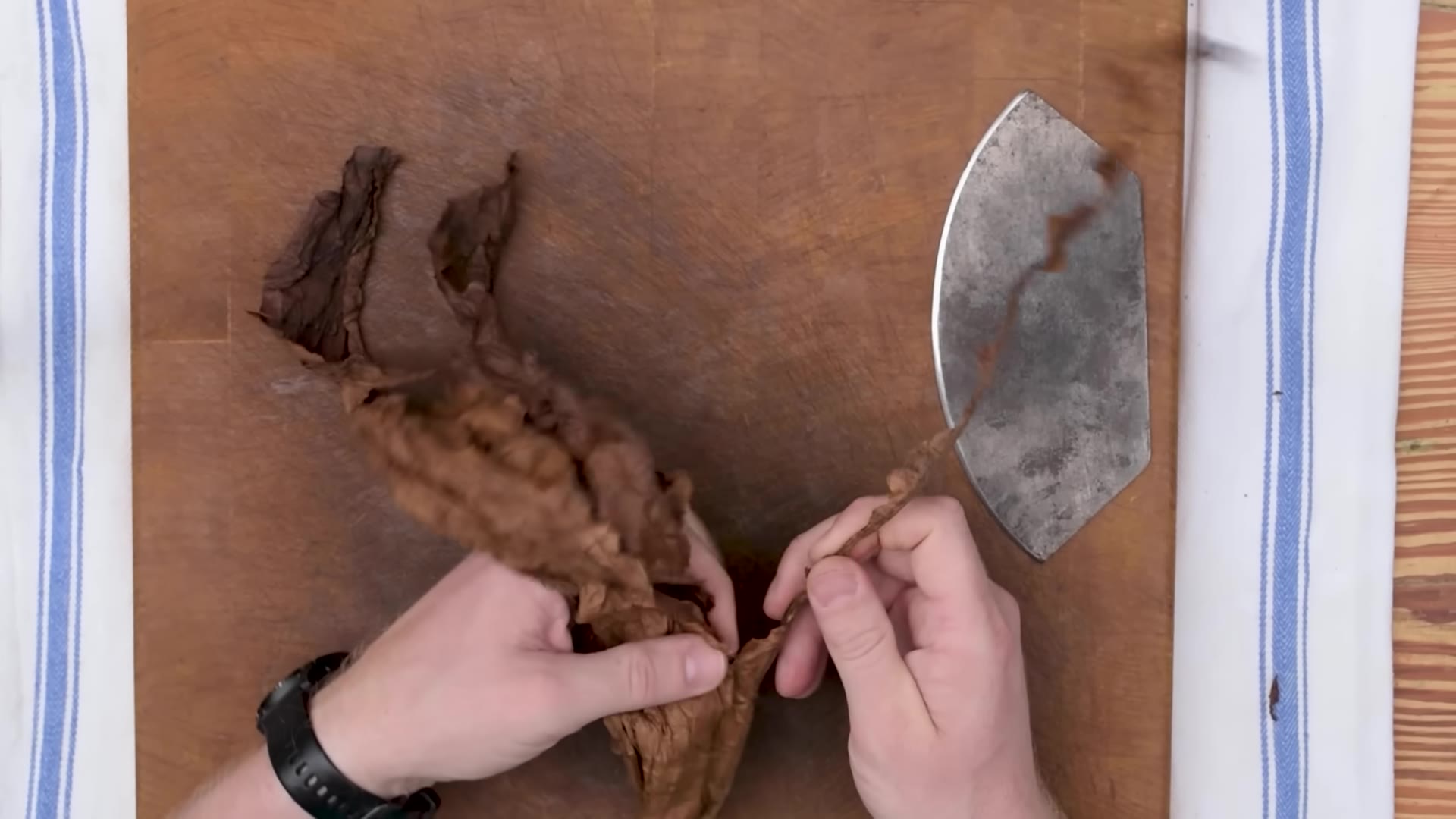 Hands folding tobacco filler leaves into a bunch on a wooden board