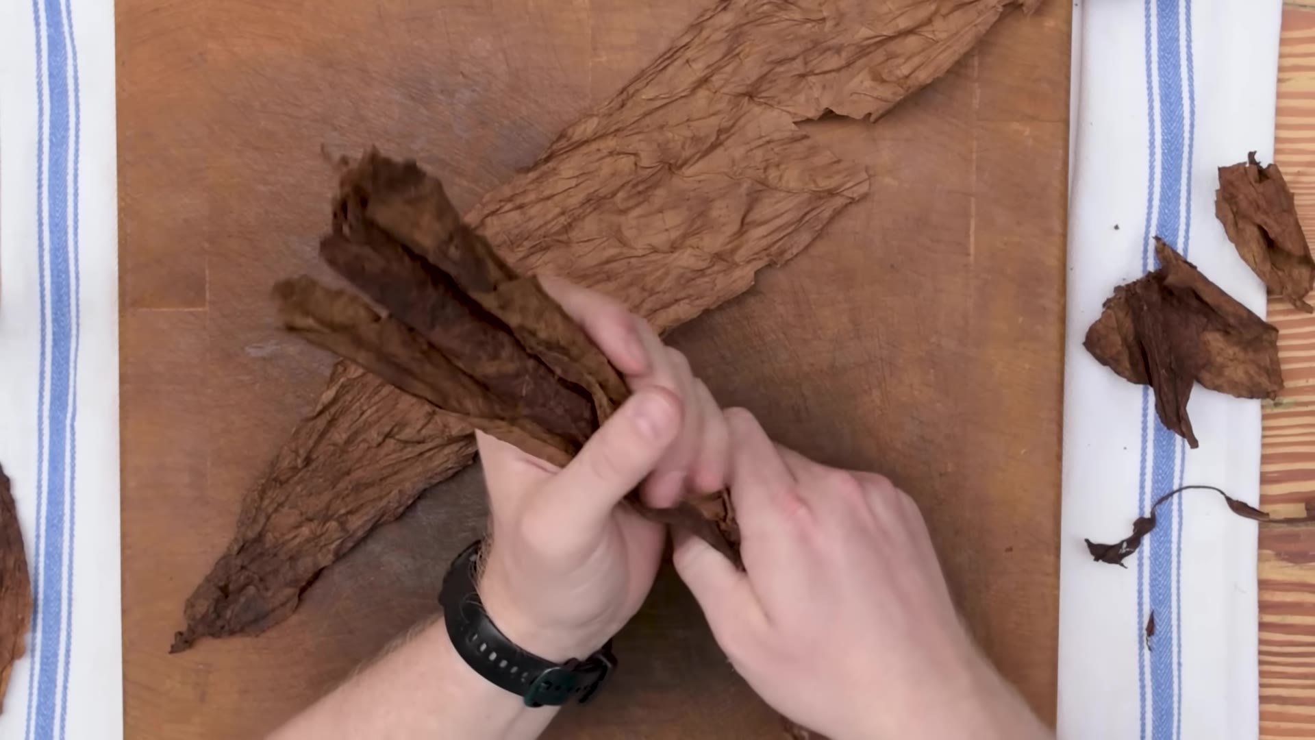 Whole long-filler tobacco leaves fanned out on a wooden board next to a chaveta blade