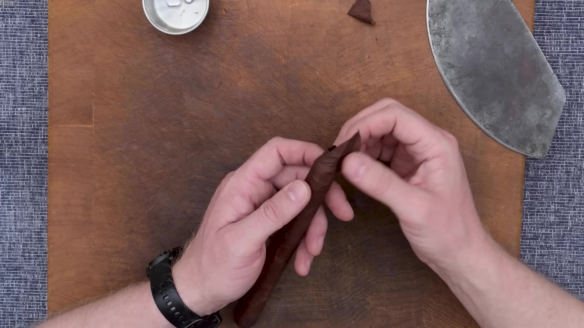 Hands pressing a small cap of wrapper leaf onto the head of the cigar, glue pot nearby